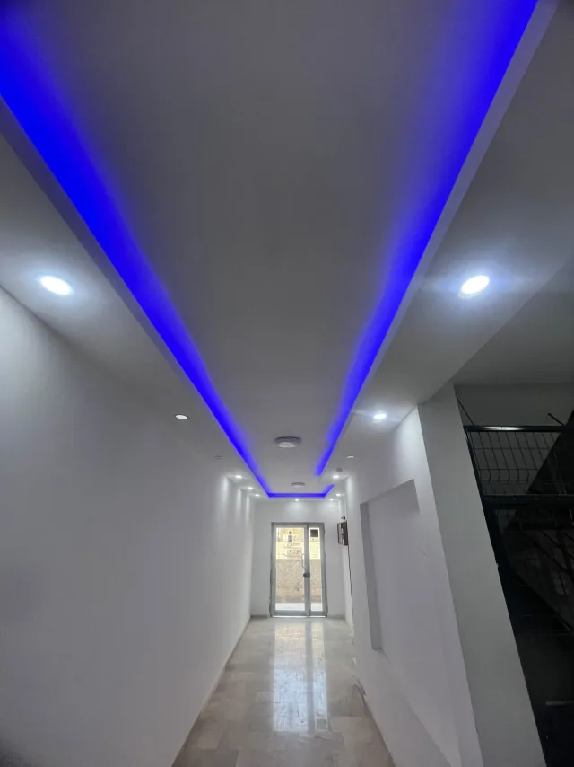 Mavi gizli LED ve beyaz spotlarla aydınlatılmış uzun apartman koridoru